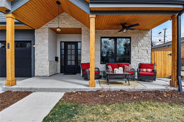 entrance to property with fence, an attached garage, ceiling fan, stone siding, and an outdoor hangout area