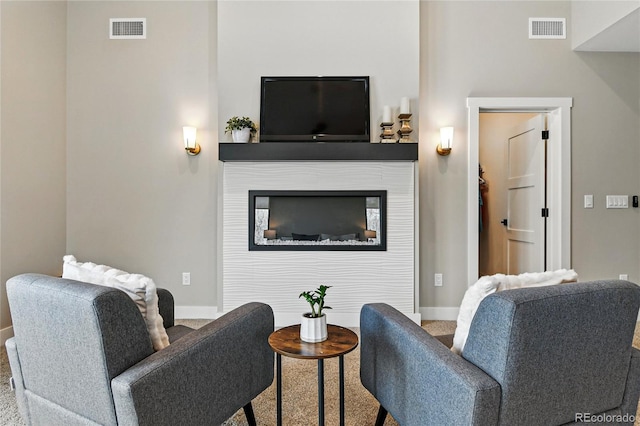 living area with a glass covered fireplace, baseboards, and visible vents