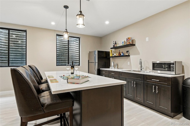 kitchen featuring a kitchen island, a breakfast bar area, appliances with stainless steel finishes, hanging light fixtures, and a sink