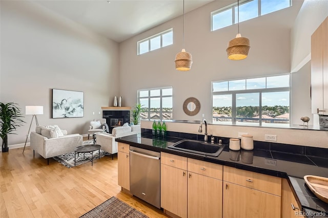 kitchen featuring a sink, light brown cabinets, stainless steel dishwasher, a towering ceiling, and a glass covered fireplace