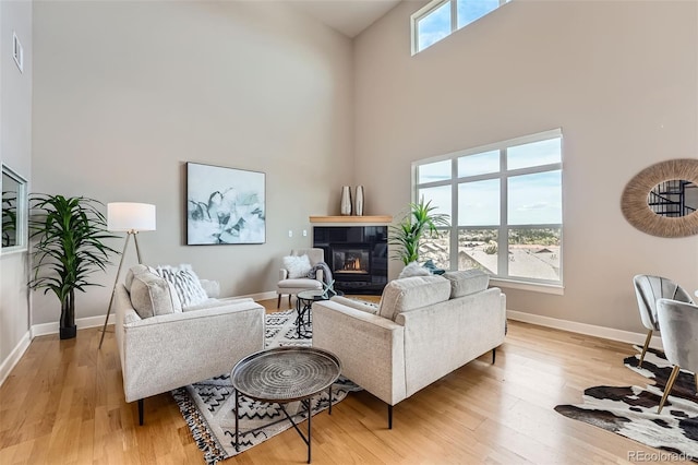 living area featuring baseboards, a tile fireplace, a high ceiling, and light wood-style floors
