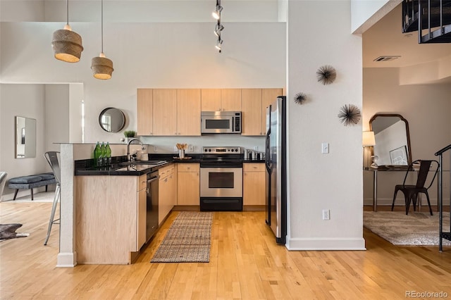 kitchen with light brown cabinetry, a peninsula, appliances with stainless steel finishes, and a towering ceiling