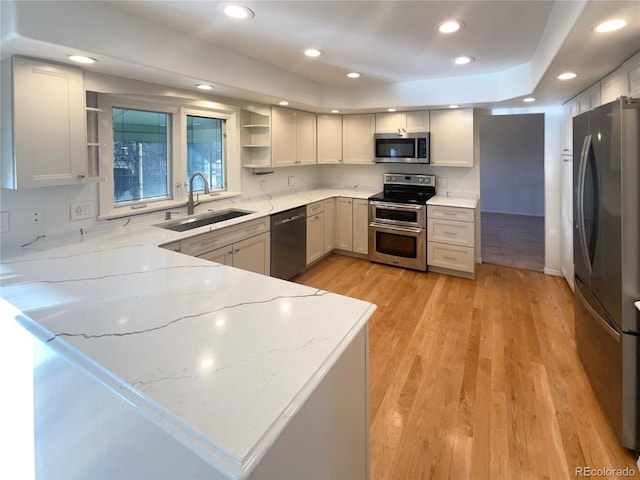 kitchen with a sink, open shelves, stainless steel appliances, light wood finished floors, and light stone countertops