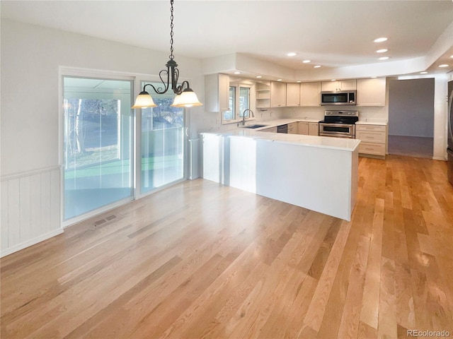 kitchen featuring visible vents, a sink, light wood-style floors, appliances with stainless steel finishes, and a peninsula