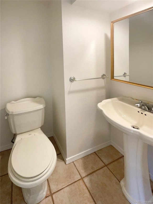 half bathroom featuring tile patterned floors, toilet, baseboards, and a sink