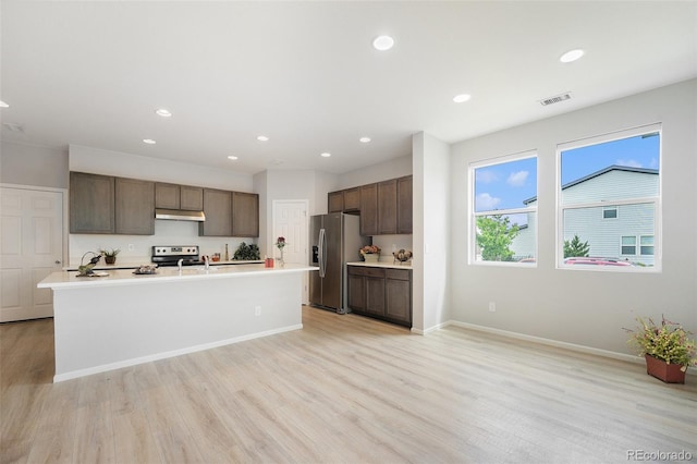 4760 Kittredge St, Denver, CO 80239 - kitchen featuring stainless steel appliances, under cabinet range hood, dark brown cabinets, light wood-type flooring, and light countertops