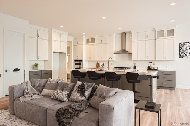 kitchen with a breakfast bar area, white cabinetry, wall chimney exhaust hood, and an island with sink