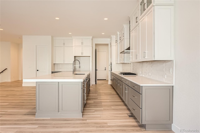 kitchen featuring backsplash, a kitchen island with sink, sink, light hardwood / wood-style flooring, and gray cabinets