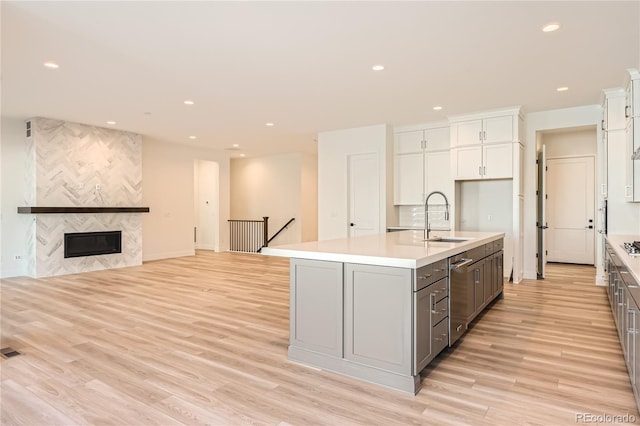 kitchen featuring a tiled fireplace, a center island with sink, light hardwood / wood-style flooring, and sink