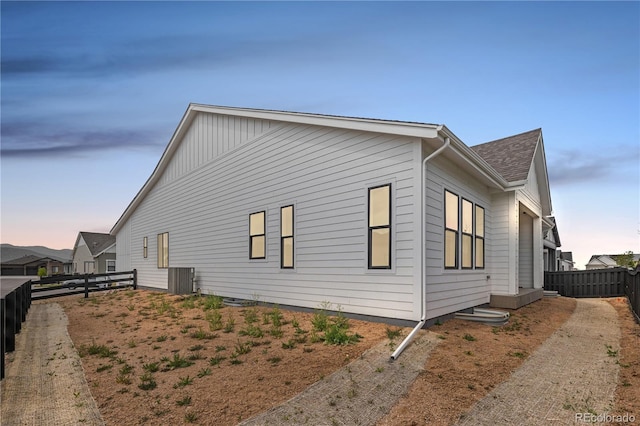 property exterior at dusk featuring a fenced backyard, roof with shingles, and cooling unit