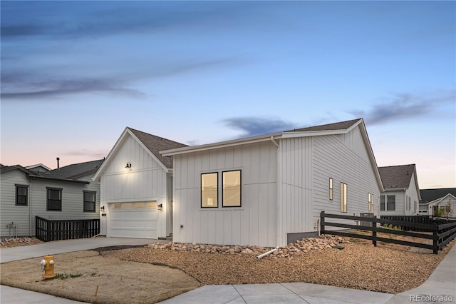 modern farmhouse style home with fence, a shingled roof, board and batten siding, an attached garage, and driveway
