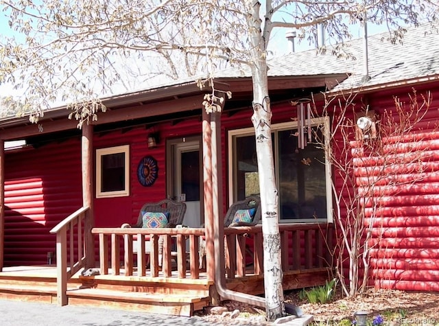 entrance to property with a porch and roof with shingles