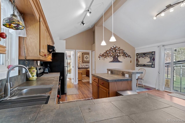 kitchen featuring track lighting, brown cabinetry, vaulted ceiling, a sink, and dark countertops