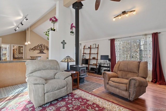 living area featuring vaulted ceiling, track lighting, a wood stove, ceiling fan, and wood finished floors