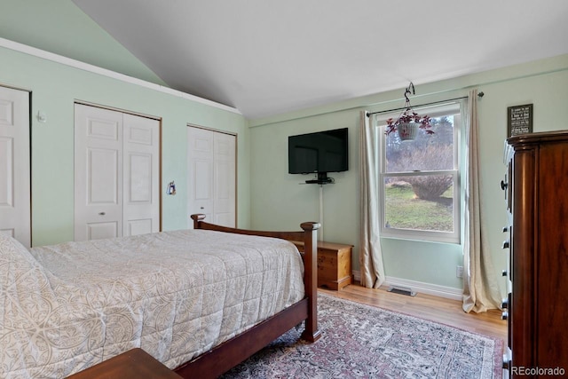 bedroom featuring lofted ceiling, baseboards, multiple closets, and wood finished floors