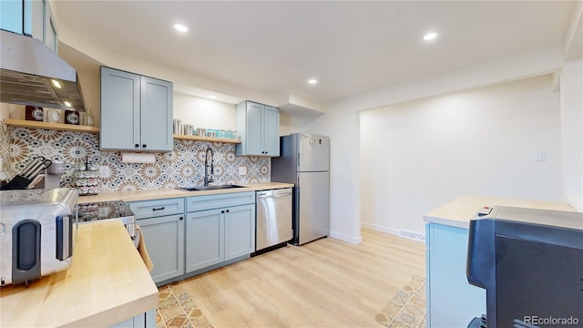 kitchen with open shelves, ventilation hood, stainless steel dishwasher, freestanding refrigerator, and a sink