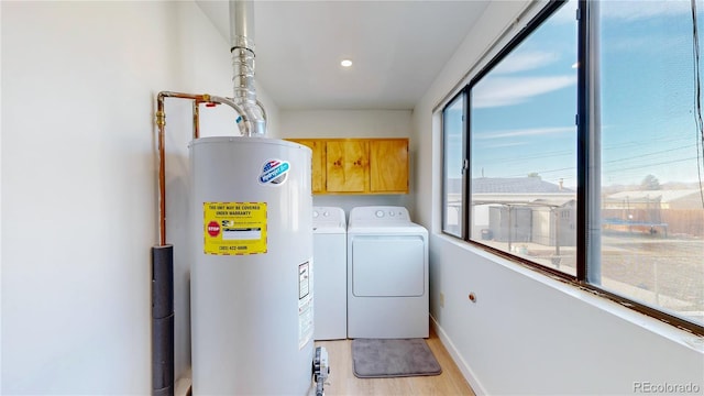 laundry area with light wood finished floors, baseboards, washing machine and dryer, water heater, and cabinet space