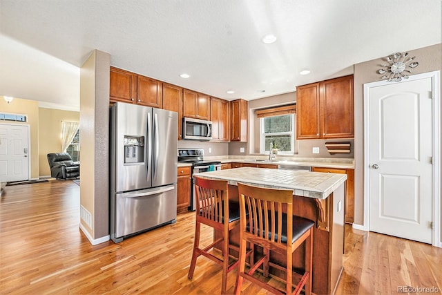 kitchen featuring brown cabinetry, stainless steel appliances, light wood-style floors, and a center island