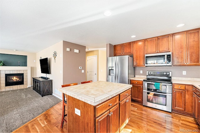 kitchen with brown cabinetry, stainless steel appliances, light wood-style floors, and a tile fireplace