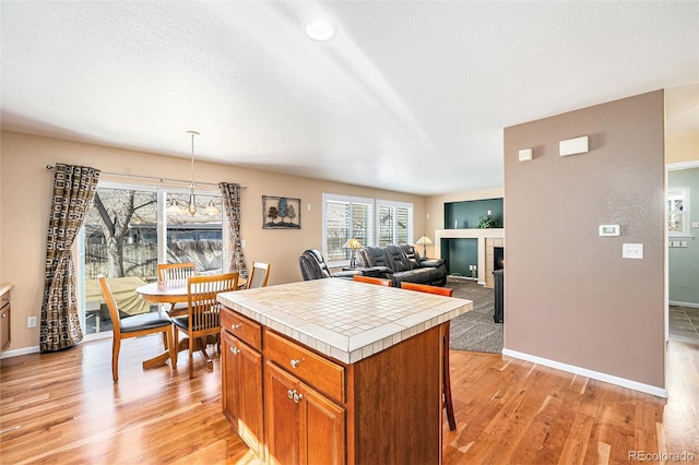 kitchen with tile countertops, brown cabinetry, a textured ceiling, light wood-type flooring, and a tile fireplace