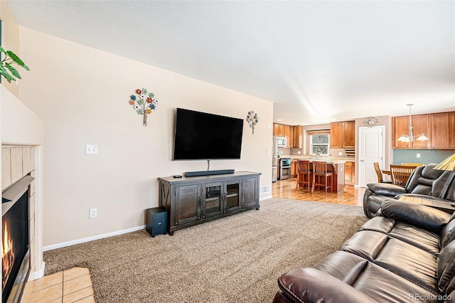 living area with a warm lit fireplace, light carpet, and baseboards