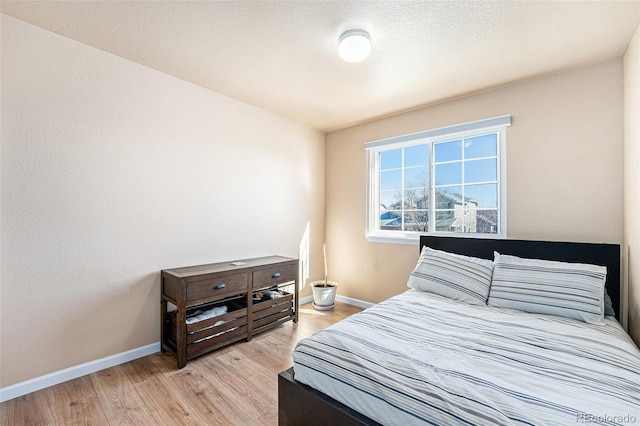 bedroom featuring light wood-style floors, baseboards, and a textured ceiling