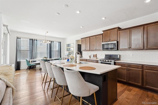 kitchen with stainless steel appliances, a sink, a kitchen breakfast bar, light countertops, and an island with sink