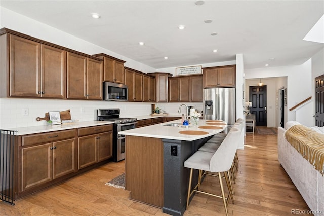 12264 Olive Way, Thornton, CO 80602 - kitchen with stainless steel appliances, backsplash, a breakfast bar, a center island with sink, and light wood-style flooring