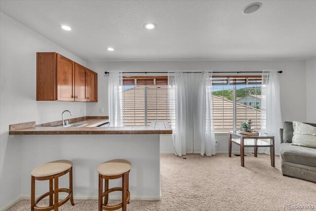 1385 Candleglow St, Castle Rock, CO 80109 - kitchen featuring light colored carpet, brown cabinets, recessed lighting, a peninsula, and a breakfast bar area