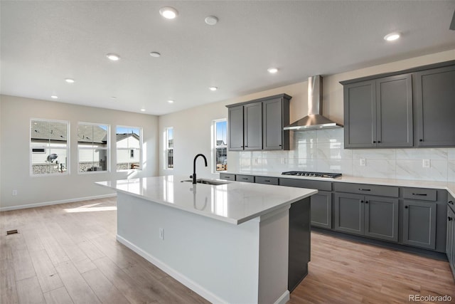 kitchen with wall chimney range hood, decorative backsplash, a sink, and gray cabinetry