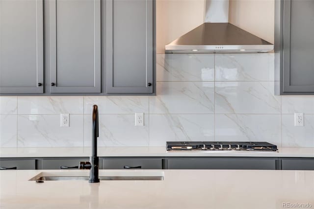 kitchen featuring stainless steel gas stovetop, gray cabinets, a sink, and wall chimney range hood