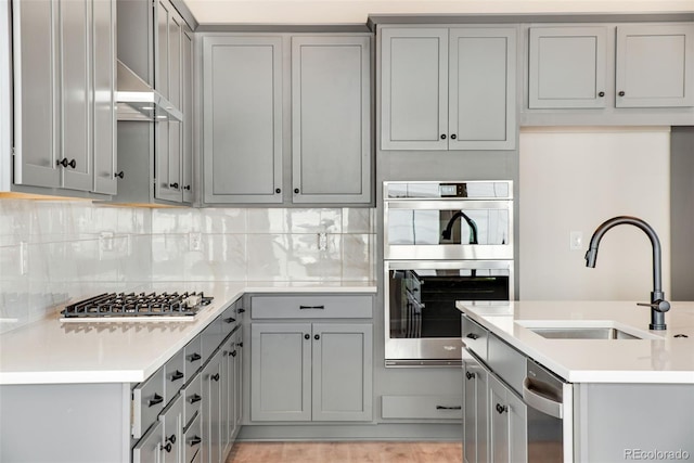 kitchen with a sink, appliances with stainless steel finishes, gray cabinets, and tasteful backsplash