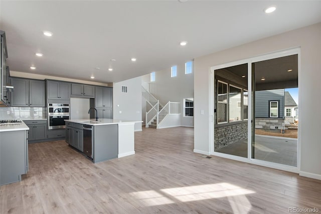 kitchen with light wood-style flooring, gray cabinetry, a sink, open floor plan, and light countertops