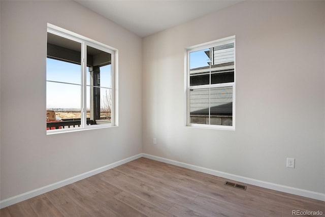 spare room with a healthy amount of sunlight, visible vents, baseboards, and wood finished floors