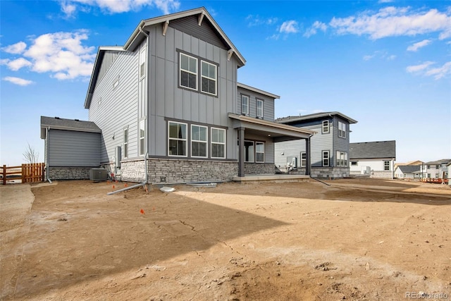 back of house with central AC unit, board and batten siding, a patio area, fence, and stone siding