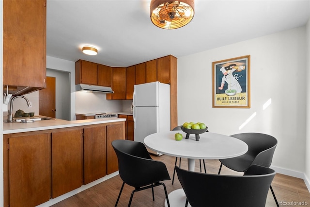 kitchen with a sink, freestanding refrigerator, light wood-type flooring, brown cabinetry, and under cabinet range hood