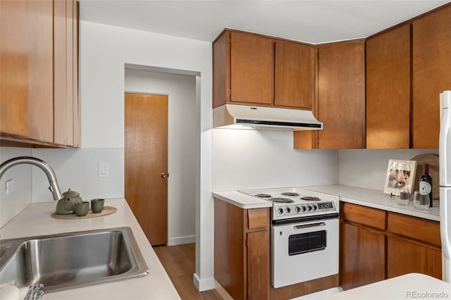 kitchen featuring white range with electric cooktop, light countertops, a sink, and under cabinet range hood