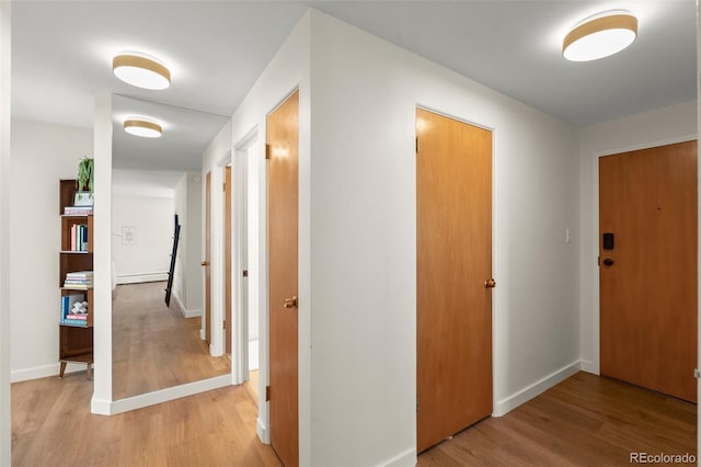 corridor with baseboards, light wood-style flooring, and a baseboard heating unit