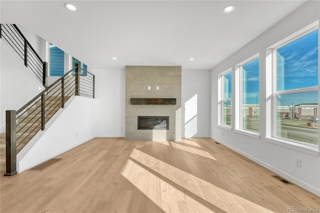 unfurnished living room with a large fireplace, wood finished floors, visible vents, baseboards, and stairway