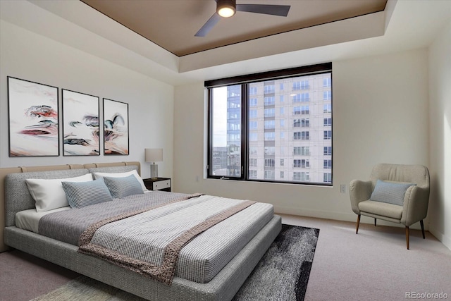 carpeted bedroom with ceiling fan and a raised ceiling