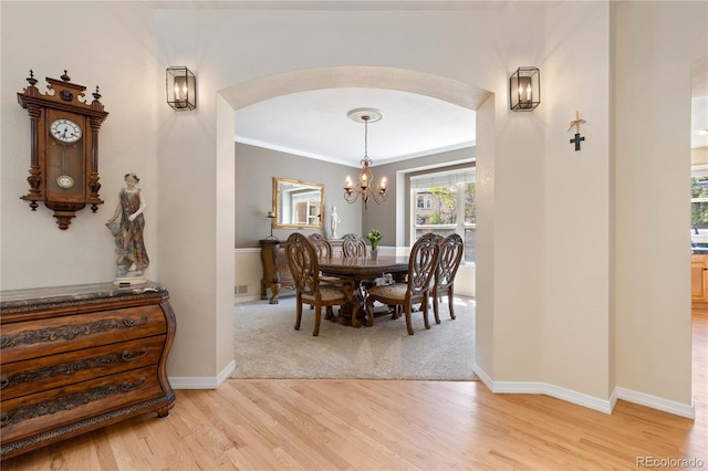 dining room featuring arched walkways, light wood-style flooring, a chandelier, baseboards, and crown molding