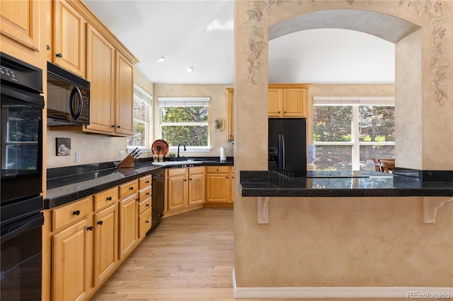 kitchen featuring light wood-style floors, black appliances, a sink, a peninsula, and a breakfast bar