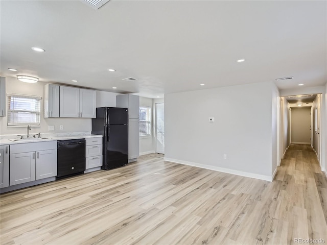 kitchen with a healthy amount of sunlight, a sink, light countertops, black appliances, and light wood finished floors