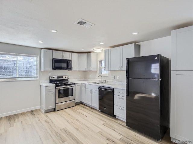 kitchen featuring visible vents, light countertops, a sink, light wood finished floors, and black appliances