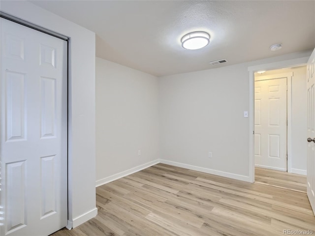 unfurnished bedroom featuring baseboards, light wood finished floors, a textured ceiling, and visible vents
