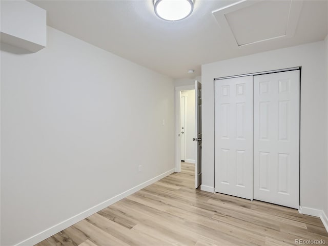 unfurnished bedroom featuring baseboards, light wood-style flooring, attic access, and a closet