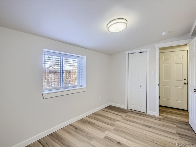 unfurnished bedroom with a closet, baseboards, vaulted ceiling, and light wood-style floors