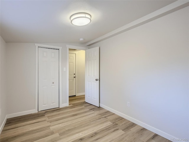 unfurnished bedroom with a closet, baseboards, and light wood-type flooring
