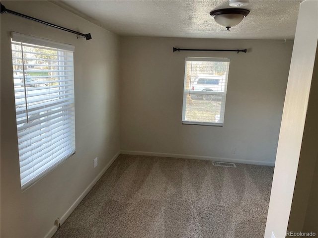 carpeted empty room featuring a textured ceiling, baseboards, and visible vents