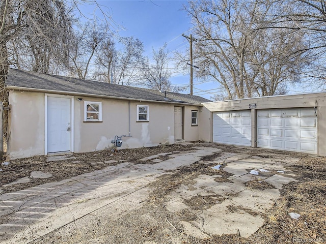 rear view of property with an attached garage, roof with shingles, stucco siding, and driveway